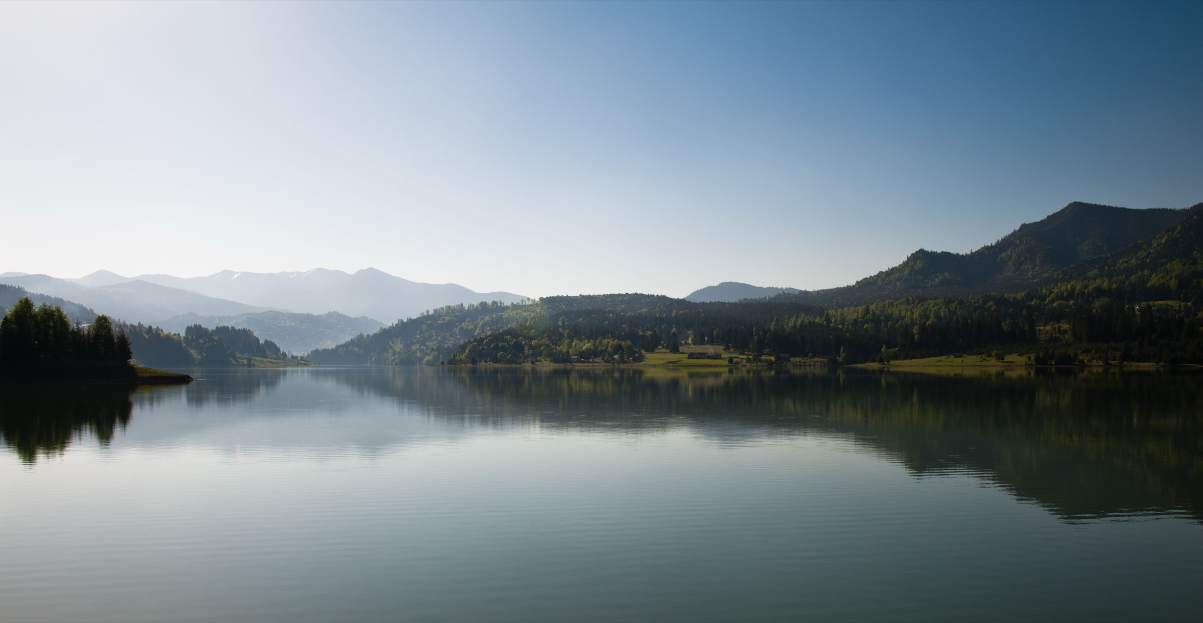 A still mountain lake at first light, ridgelines fading into haze