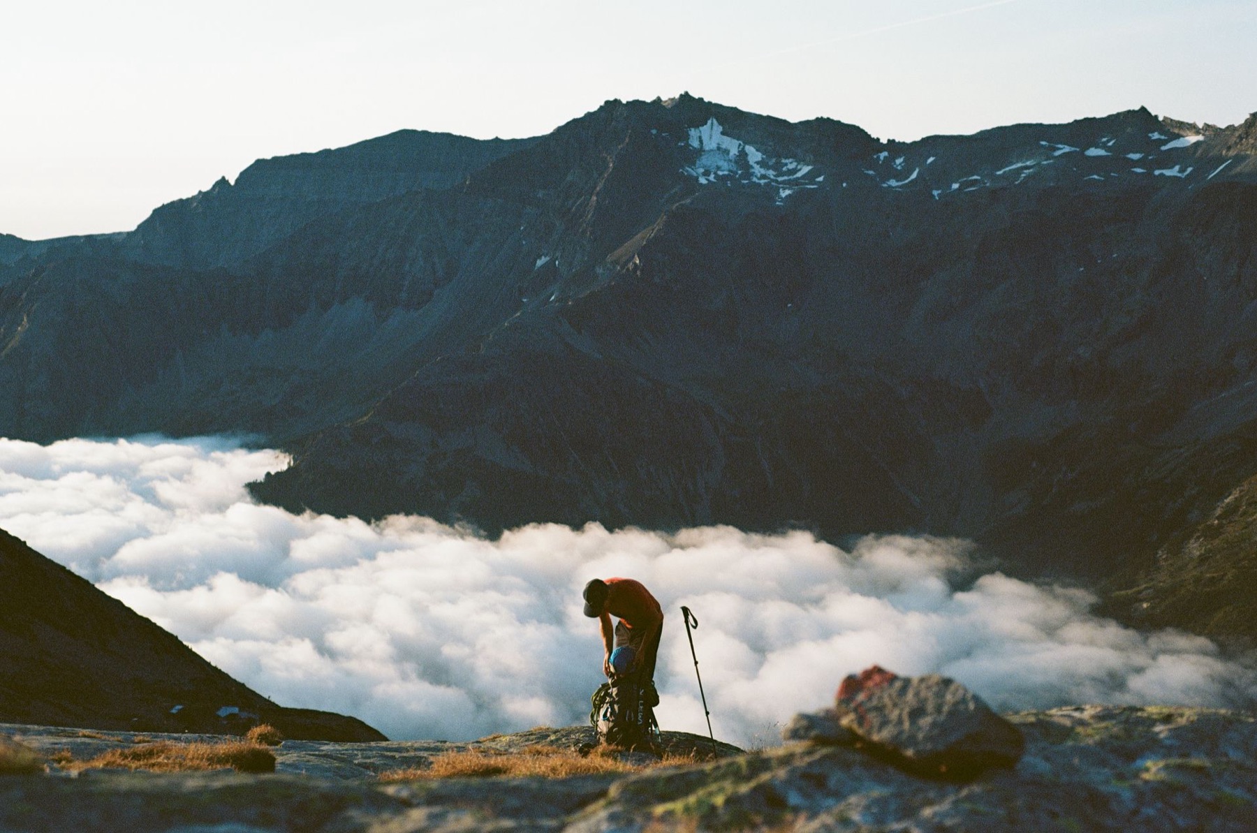 A hiker packing up on a mountain ridge above a sea of clouds