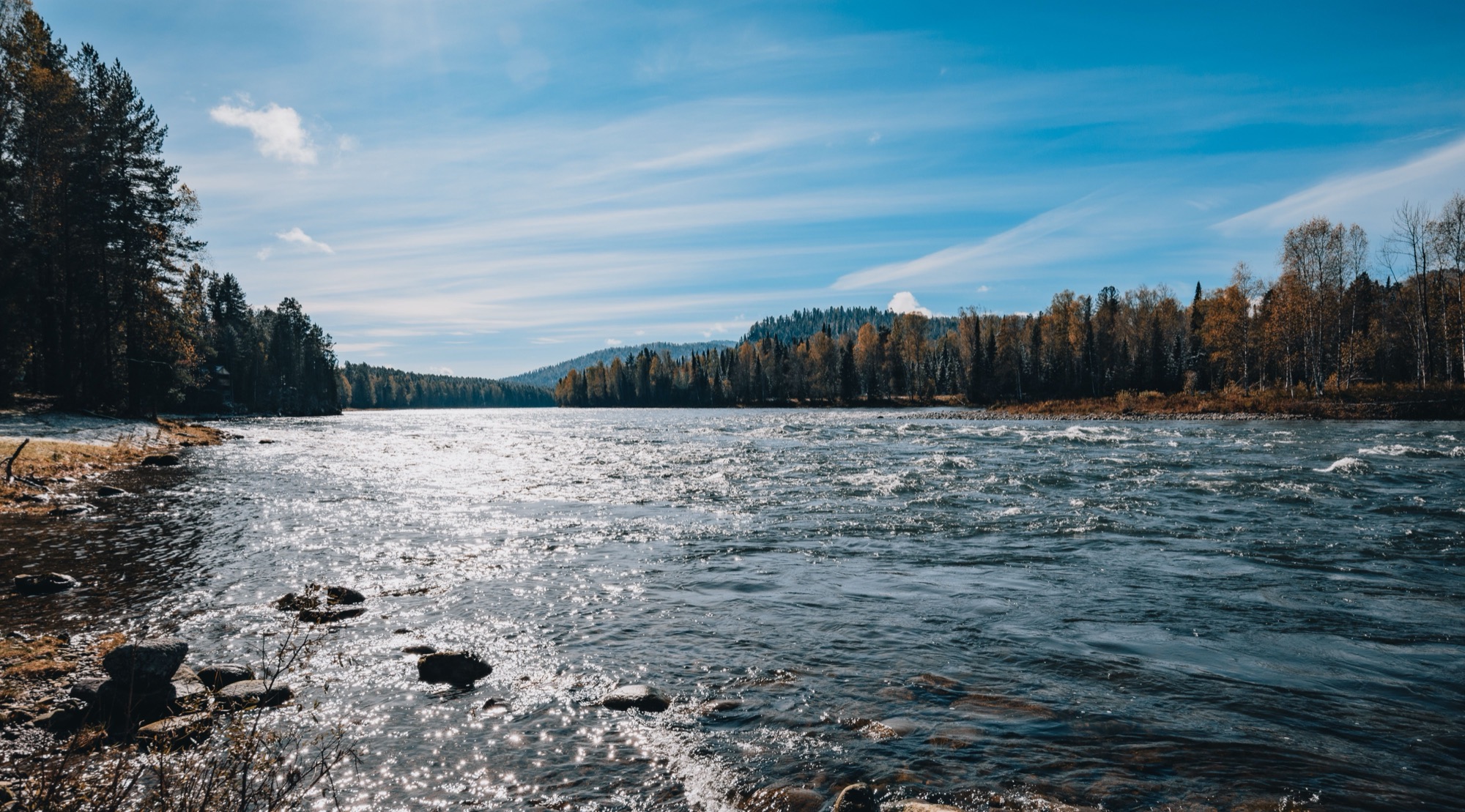 A wide river running between evergreen banks under a bright sky