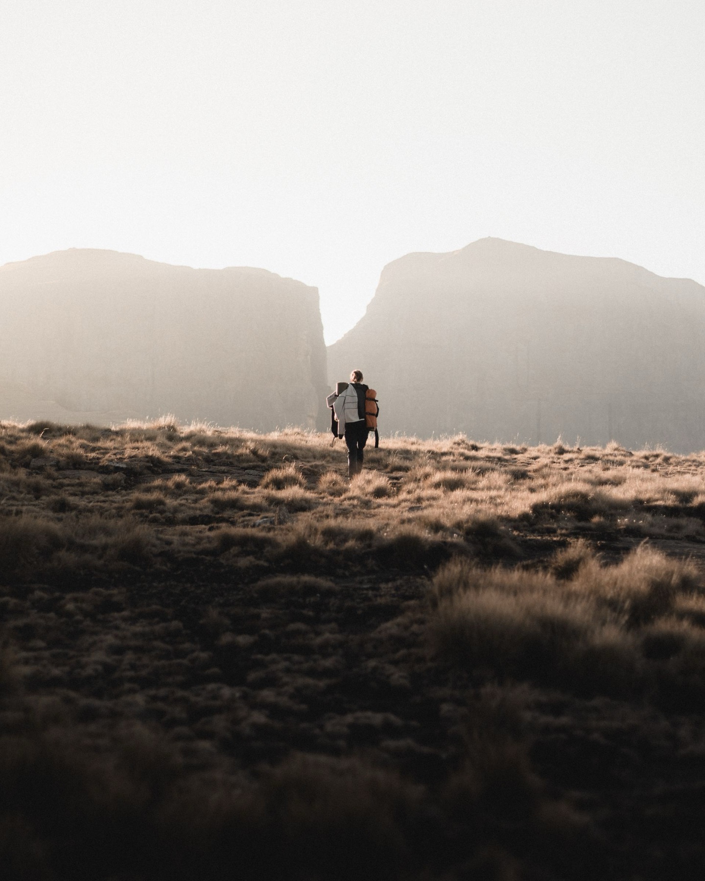 A hiker crossing an open field toward distant cliffs at first light
