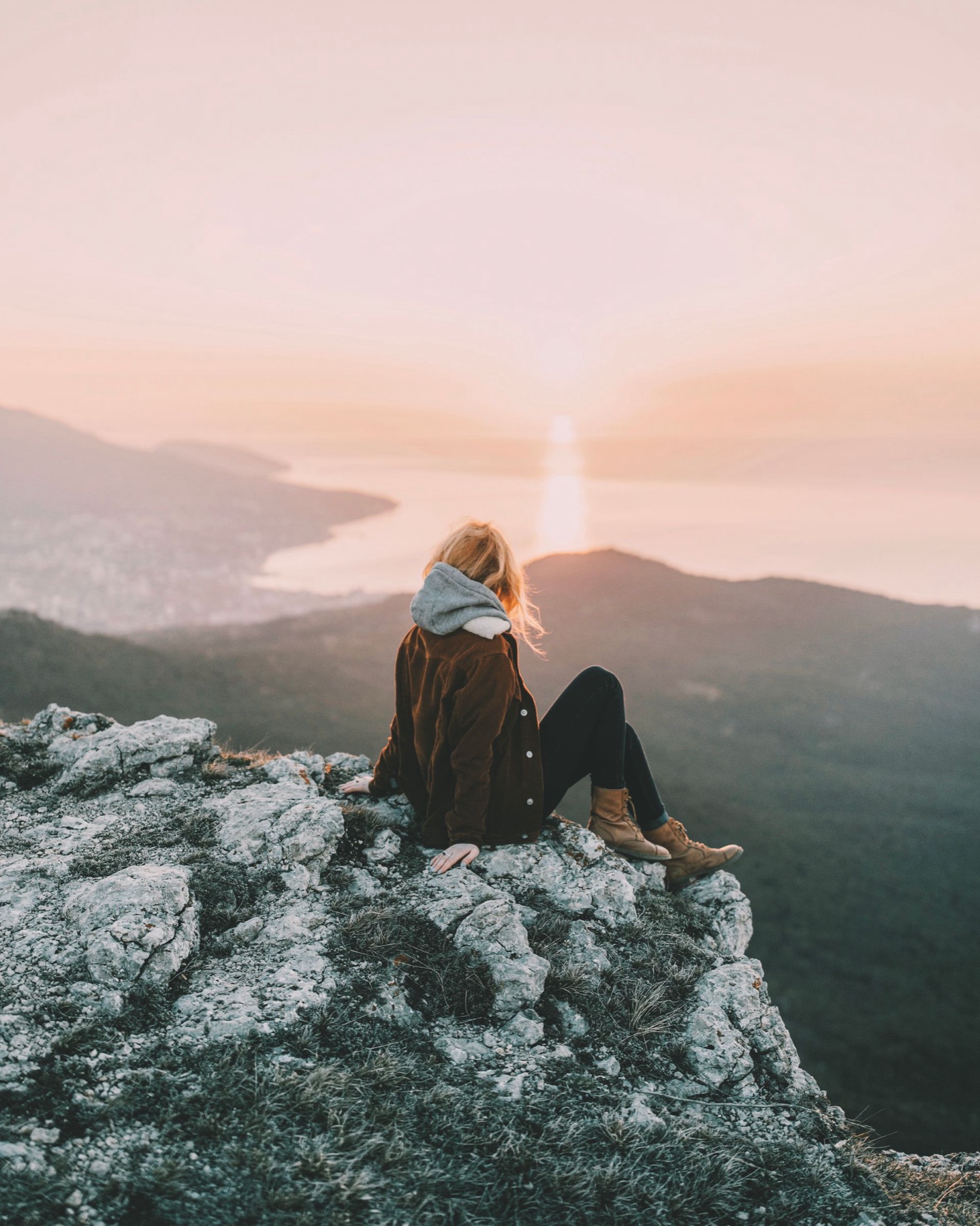 A person sitting on a rocky outcrop above a lake at sunrise