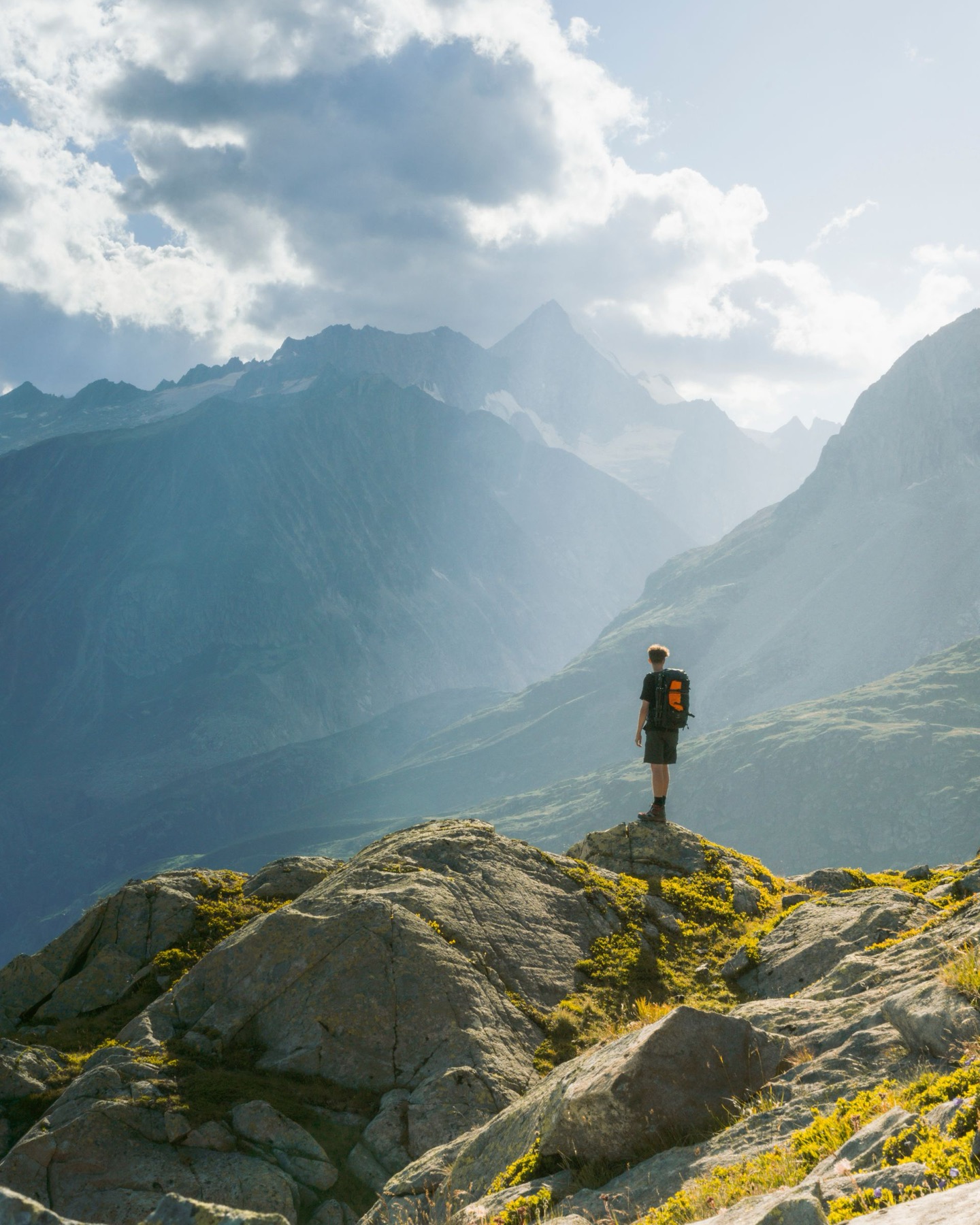 A lone hiker standing on a ridge, looking out over sunlit mountains